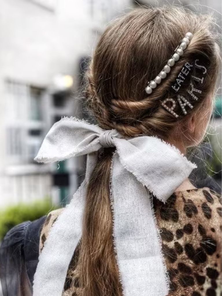 Brunette woman with a low ponytail with pearl hair clips and a hair bow