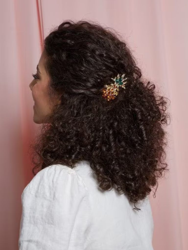 Brunette with naturally curly hair in a half-updo with a pineapple clip