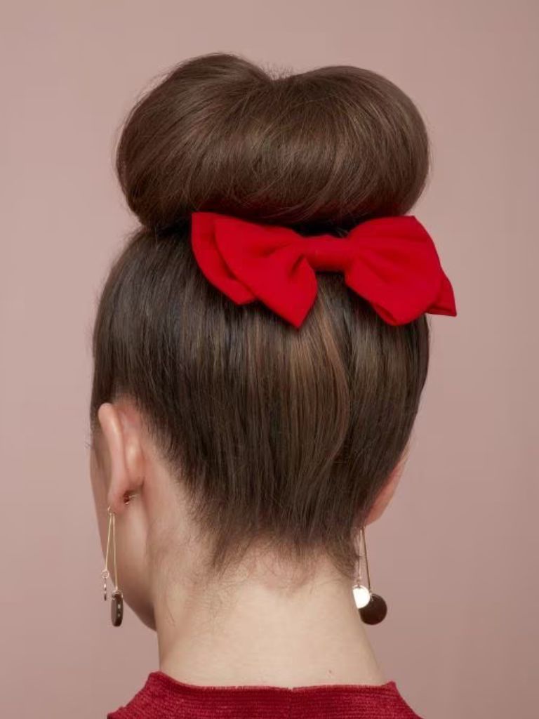 Woman with dark hair styled into a bun with red hair bow