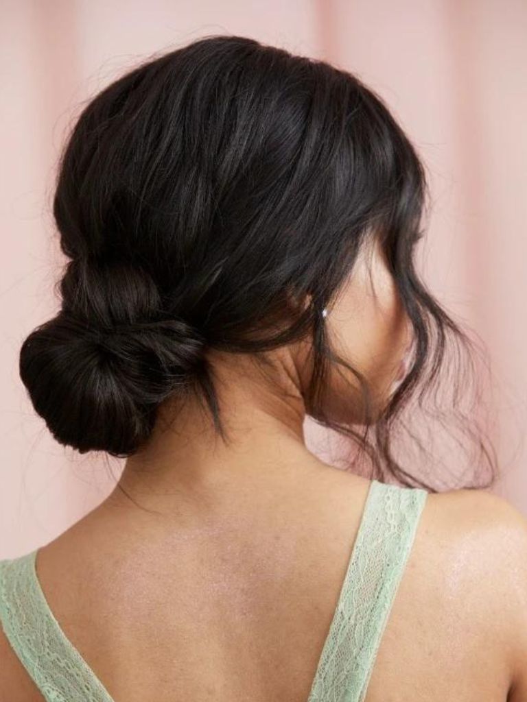 Dark haired woman with a classic low bun with curly face-framing pieces