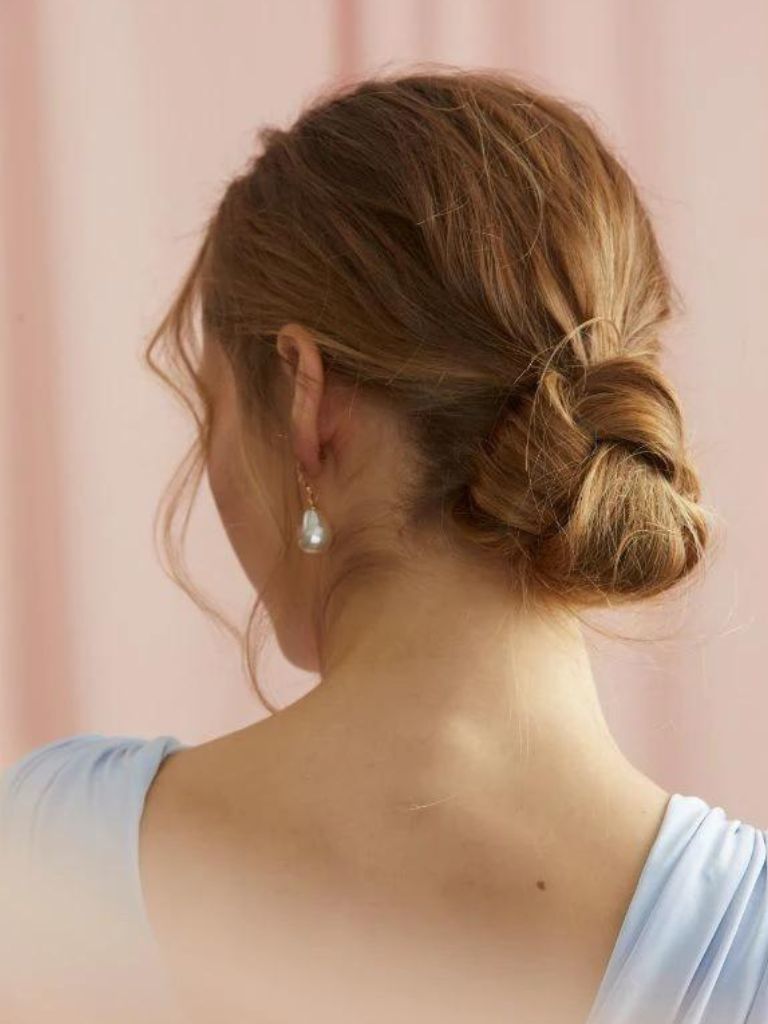 Woman with light brown hair in a knotted chignon hairstyle with curled pieces of hair