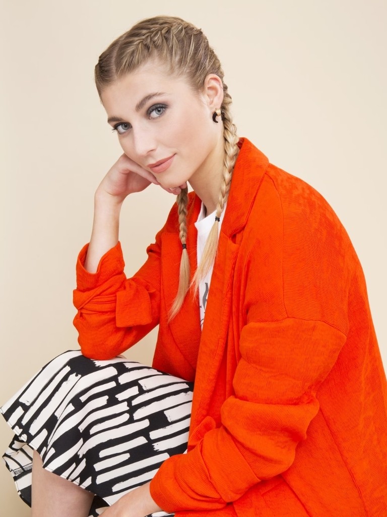 Woman in an orange jacket with hair in two french braids