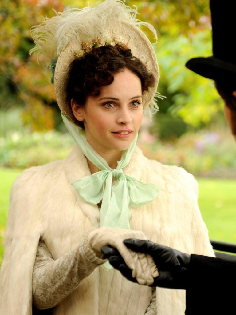 Victorian hairstyles: Close-up of Felicity Jones in Hysteria dressed in Victorian period dress with curly dark hair in an updo with a feathered hat