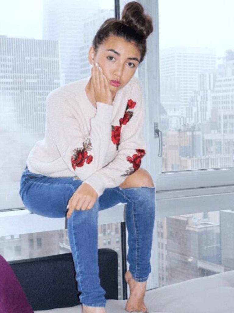 Club hairstyles: Front view image of a woman with dark hair in a top knot sitting down