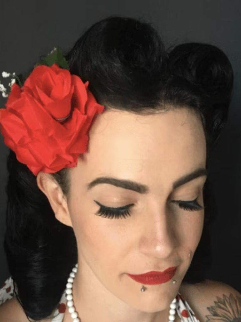Club hairstyles: Close-up of a woman with dark brown black hair in a vintage victory roll updo with a big red flower clip