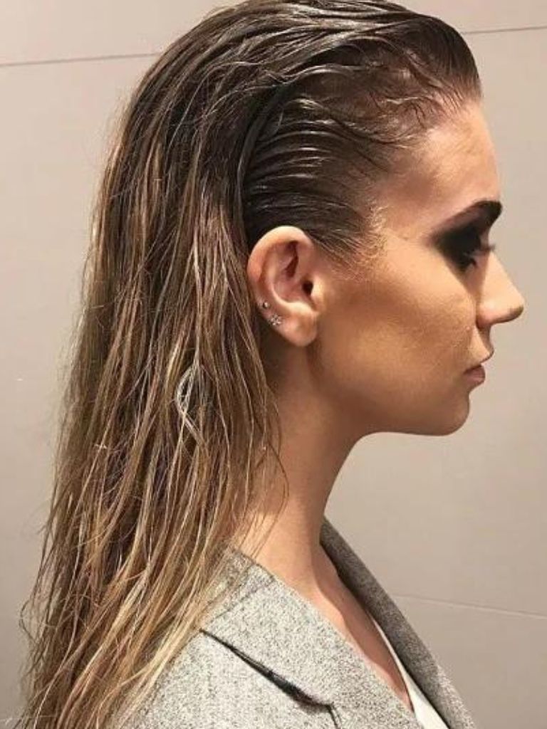Club hairstyles: Side profile shot of a brunette woman with wet look slicked back hair, wearing dark eye make-up and a grey blazer