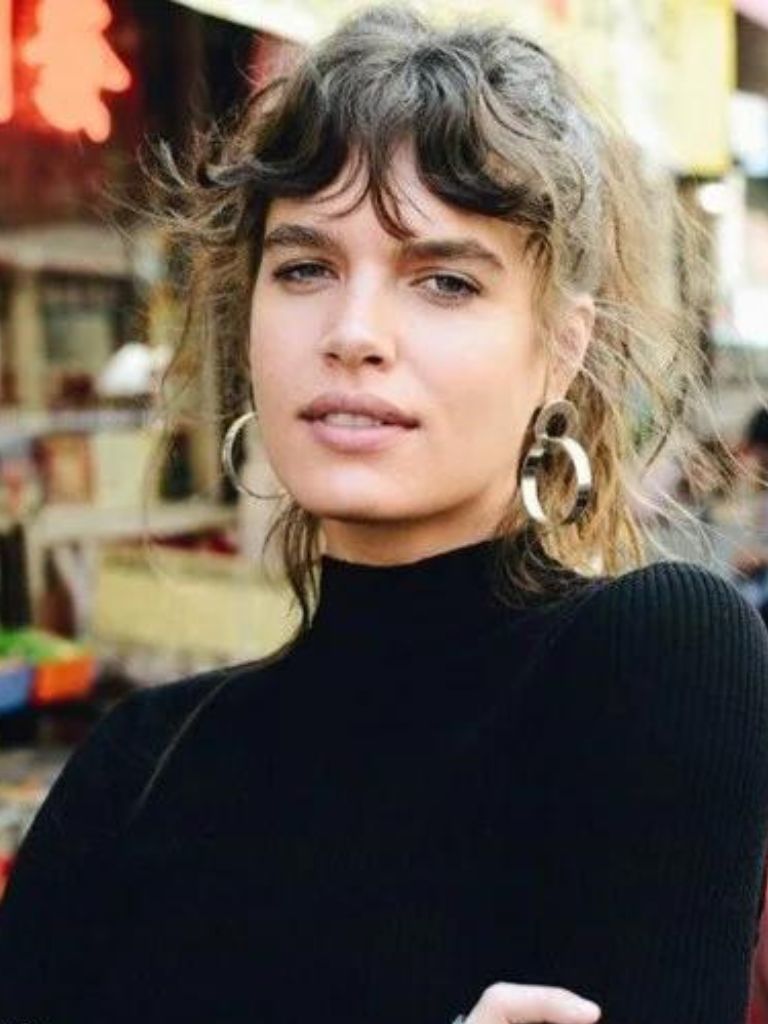 close up shot of woman with wispy bardot bangs, wearing black top and posing on the street