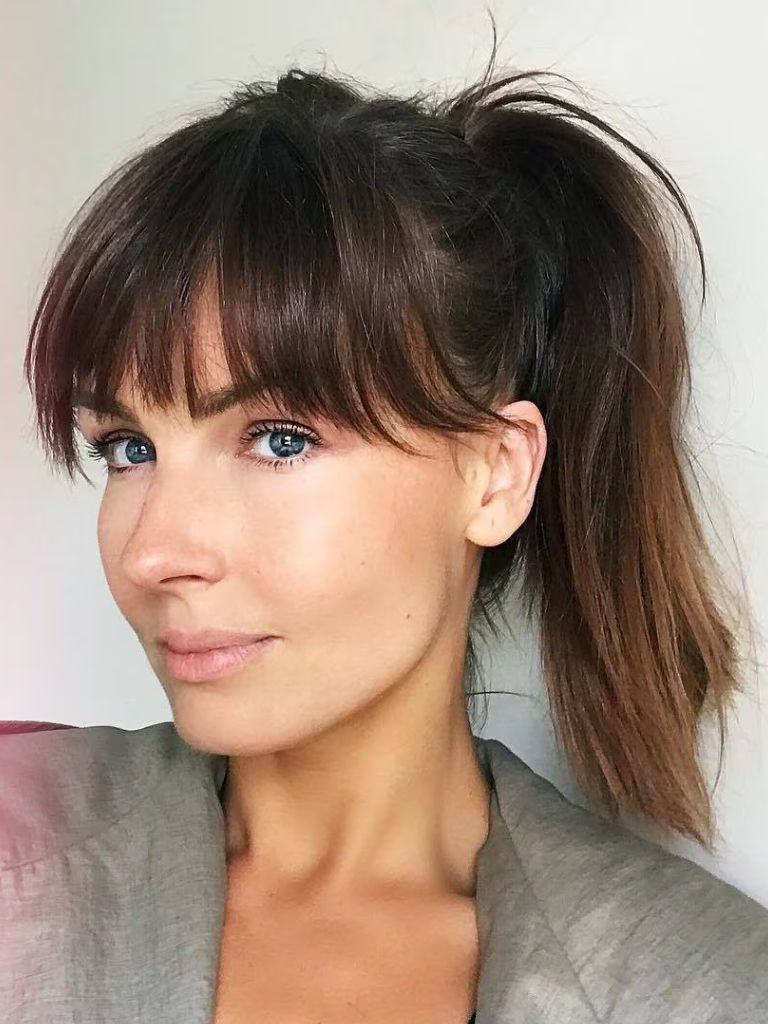 Woman with hair styled into a ponytail with wispy hair bangs