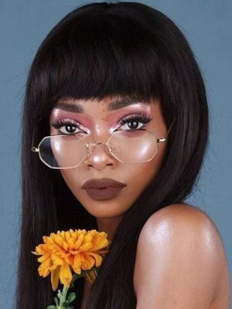close up shot of woman with straight bangs with wispy ends, wearing glasses and holding flower