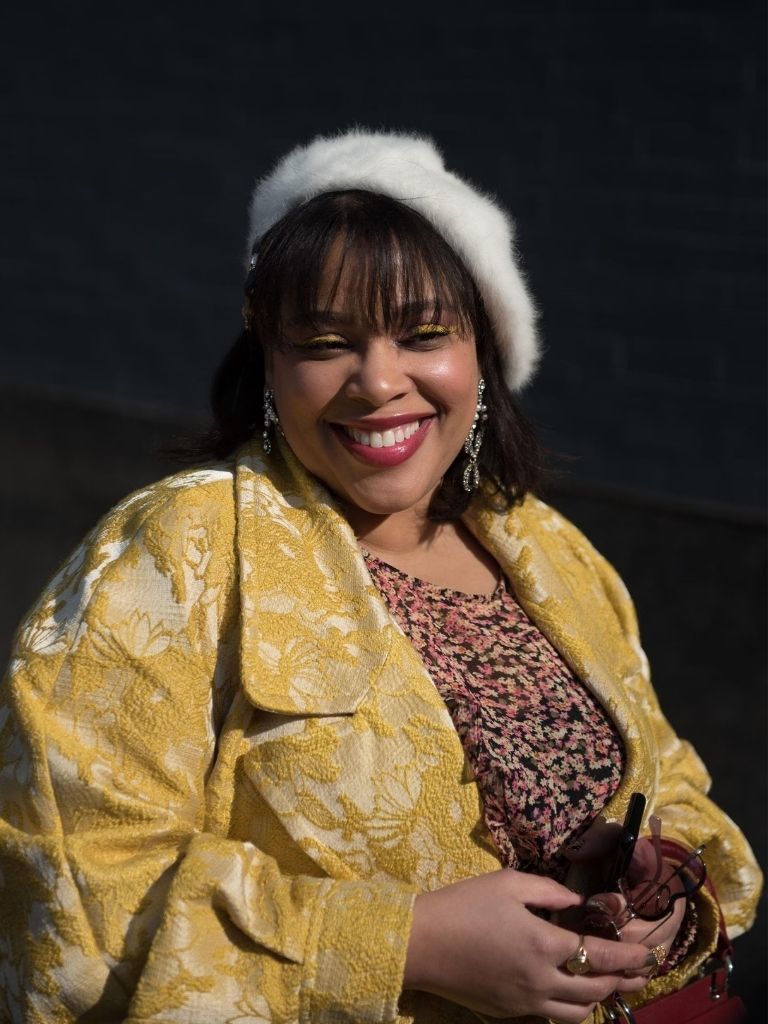 Smiling woman with a dark brown bob with a fringe, wearing a white fluffy beret
