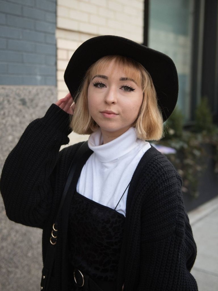 Woman with a blonde bob with blunt bangs wearing a black floppy hat