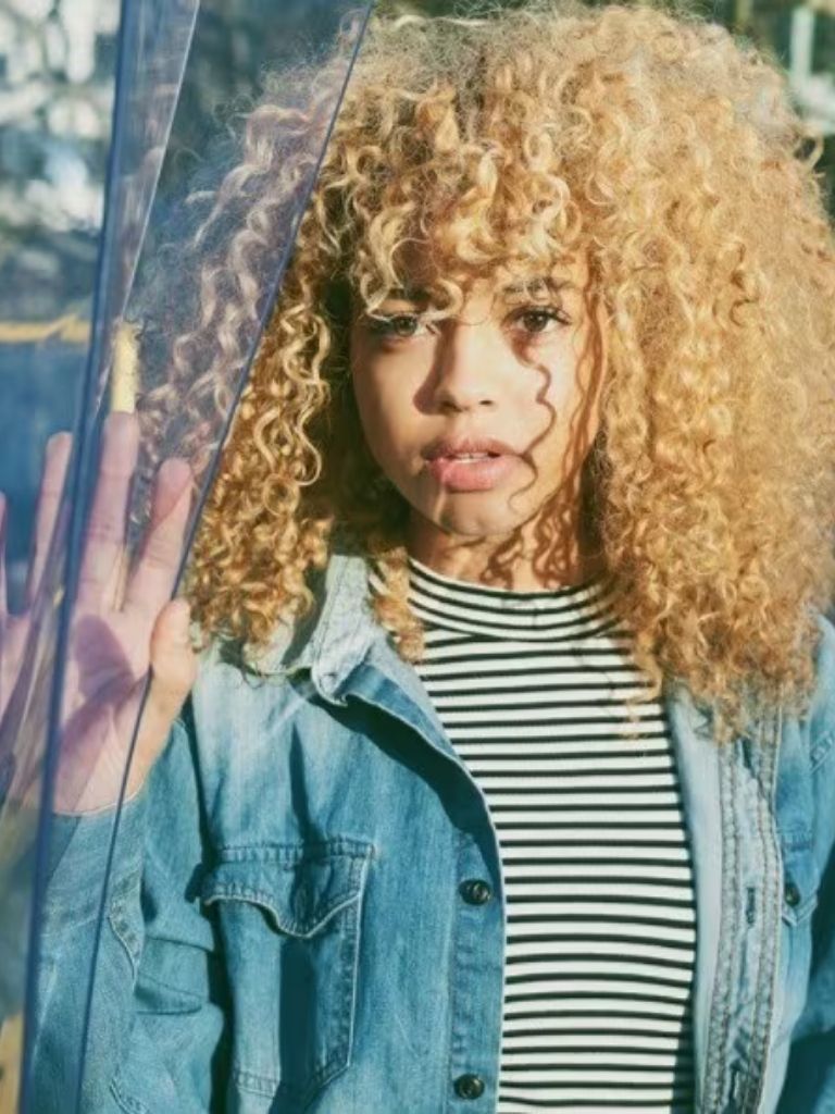 blonde natural haired woman with a full fringe wearing a denim jacket and striped tshirt