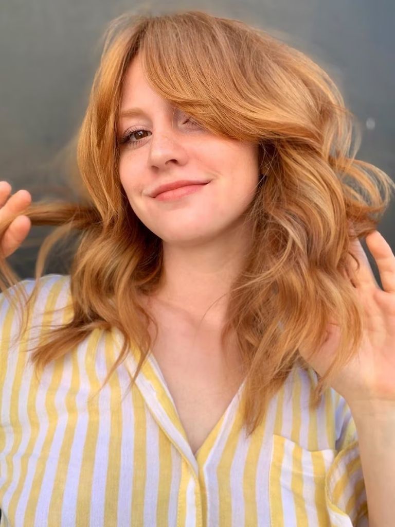 Woman with long strawberry blonde wavy hair with long bangs