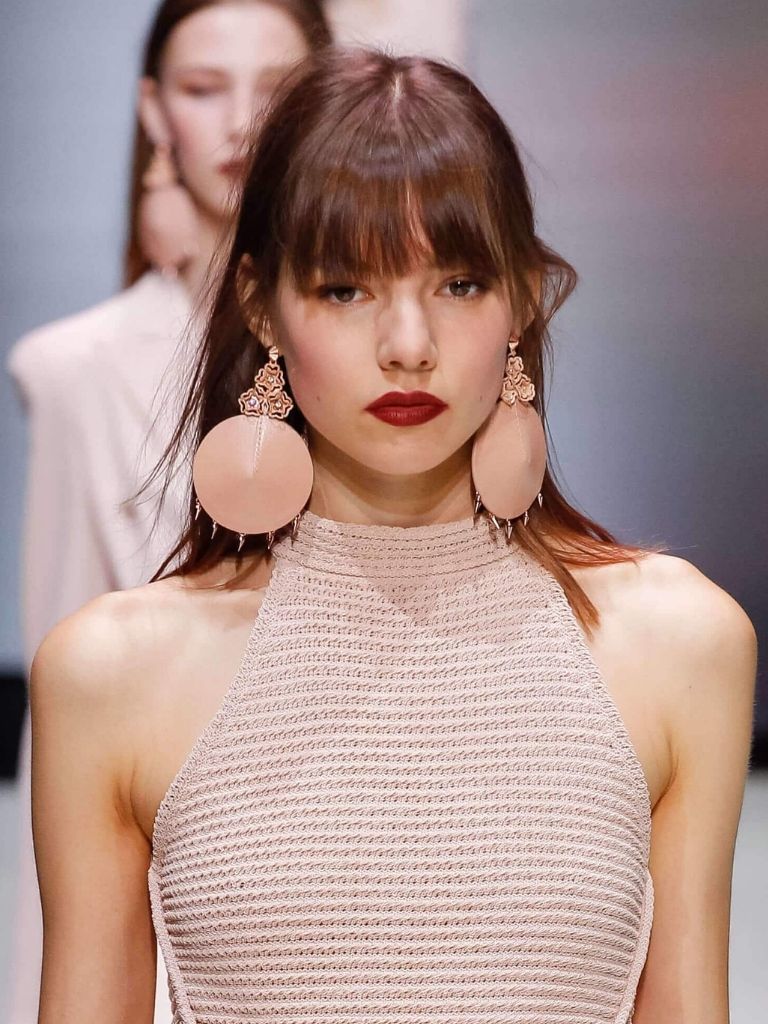 woman on the runway with a long fringe hairstyle wearing a pastel pink outfit