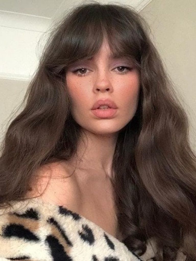 Types of bangs: Woman with long chestnut brown wavy hair with Bardot bangs, wearing a leopard print jacket