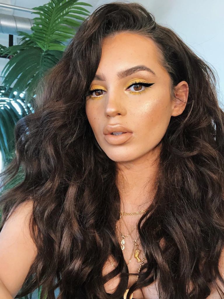 Woman with dark brown curly hair with yellow eyeshadow and winged eyeliner.