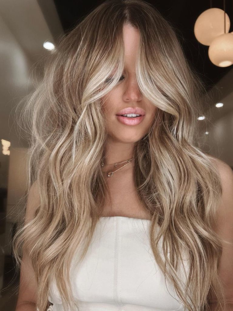 Woman with bronde balayage with gold jewellery and a white strapless top.