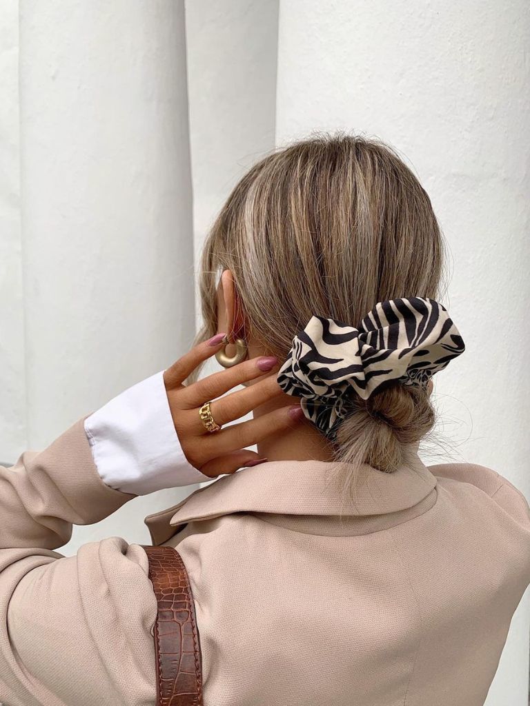 Woman with highlighted brown hair wearing a low bun with a big scrunchie.