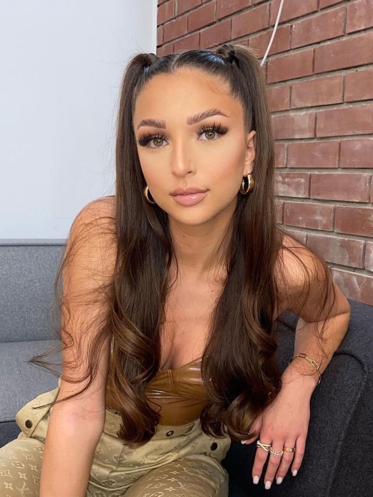 Woman with medium brown, half up pigtails sitting on a sofa.