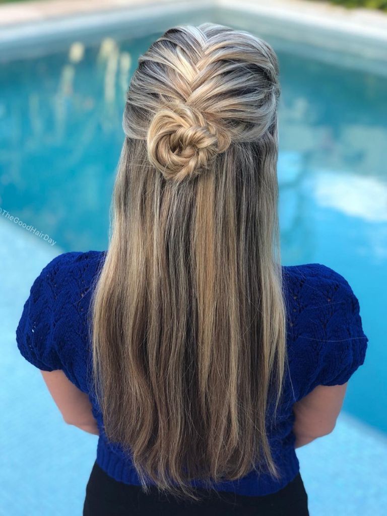 Woman sitting in front of pool with long bright blonde styled with a french fishtail braid half-up bun.