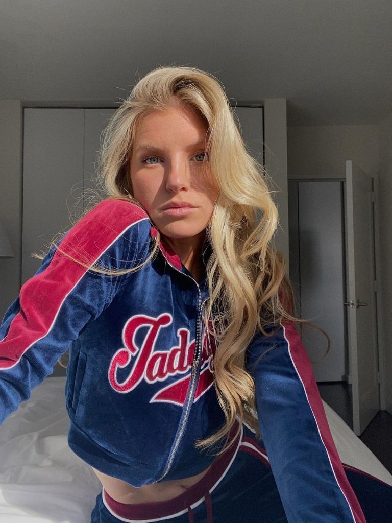 Woman with long blonde hair with a wavy 90s-style blow out wearing a blue velour tracksuit.