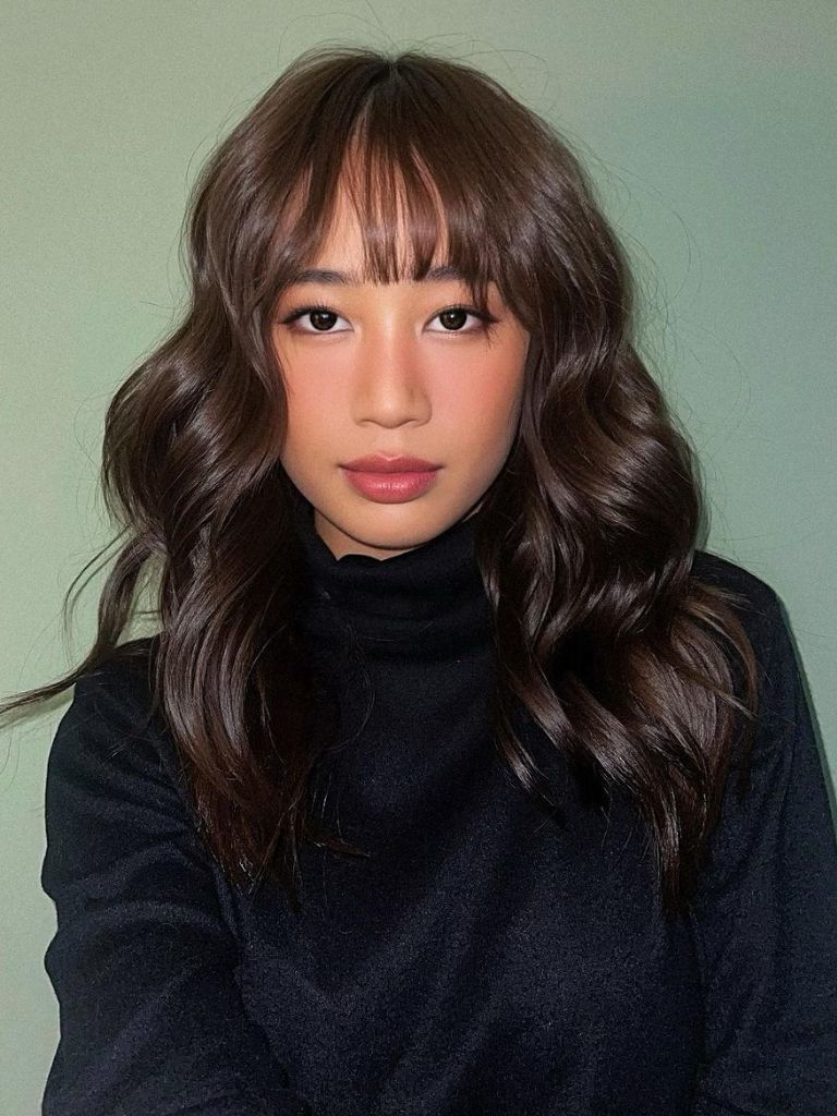 Hairstyles for long thin hair: Woman with dark brown curled hair and wispy bangs.