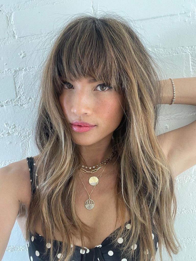 Woman with light brown and blonde highlighted hair with layers and full bangs.