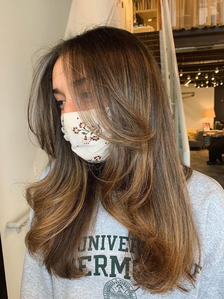 Woman with medium chestnut brown hair with long layers and babylights.