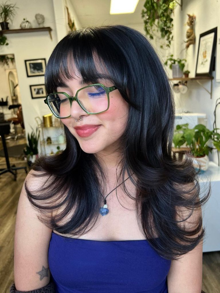 Woman with black hair, cute block bangs and bouncy layers.