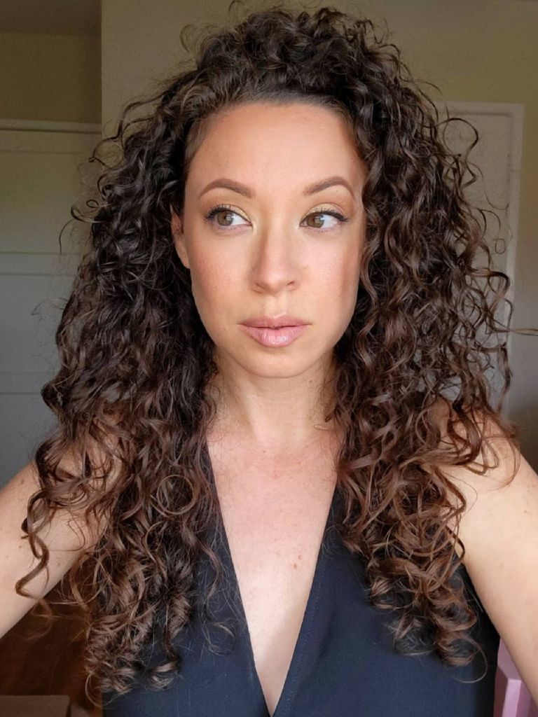 Woman with long fine dark brown curls wearing a black top.