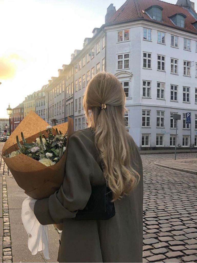 Woman with blonde hair with half clipped up holding flowers.