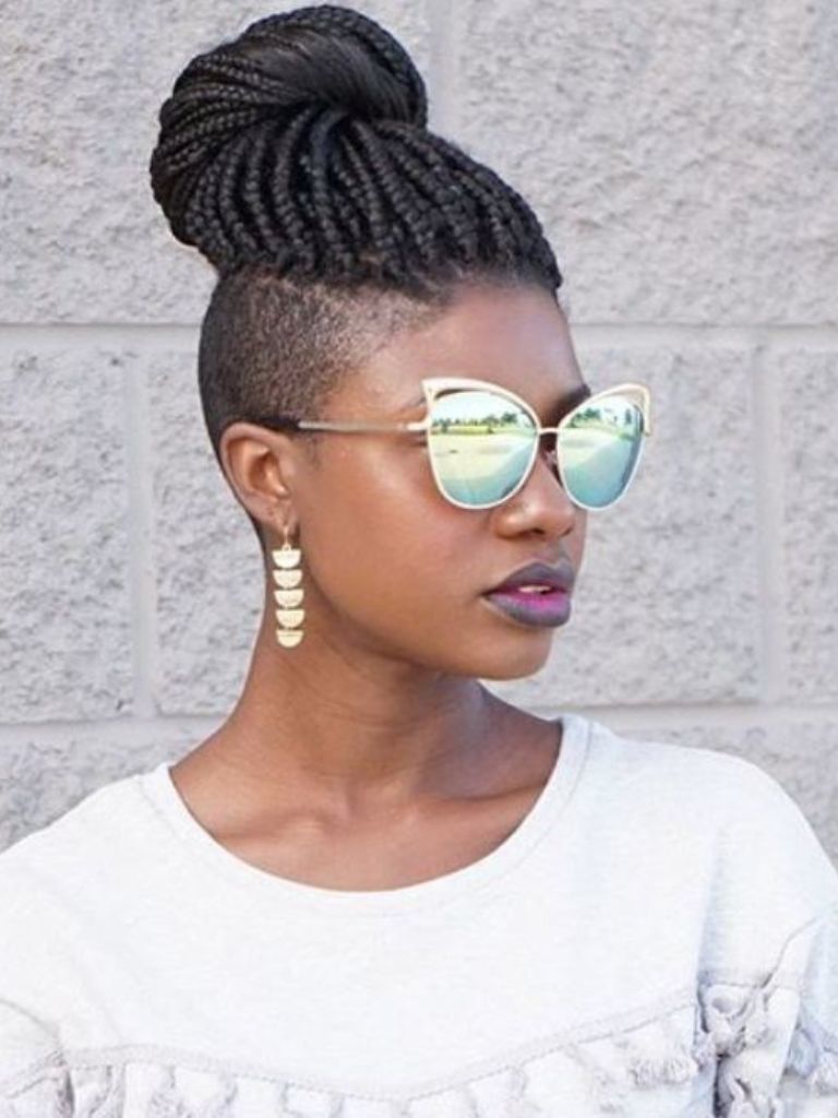 Side shot of woman with box braids with shaved sides hairstyle, wearing sunglasses, gold dangly earrings and white jumper.