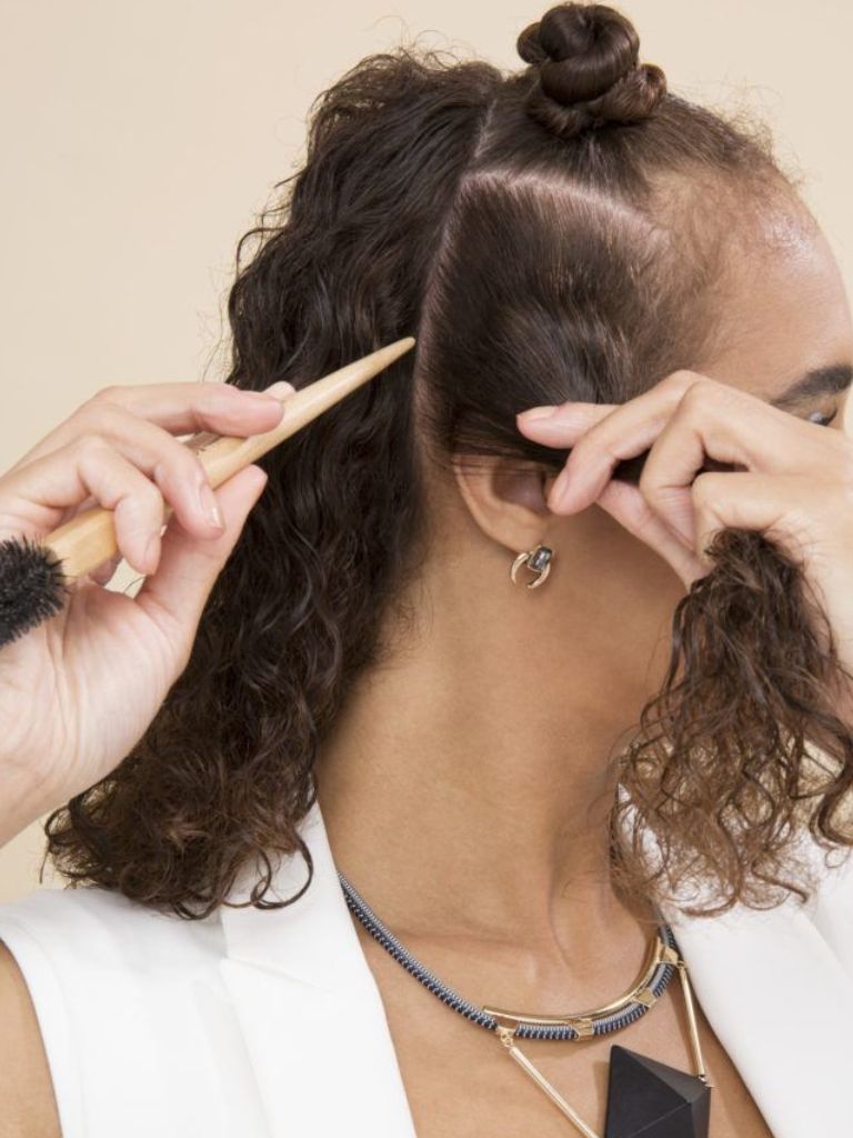 Woman with natural curly hair using the end of a brush to section her hair.
