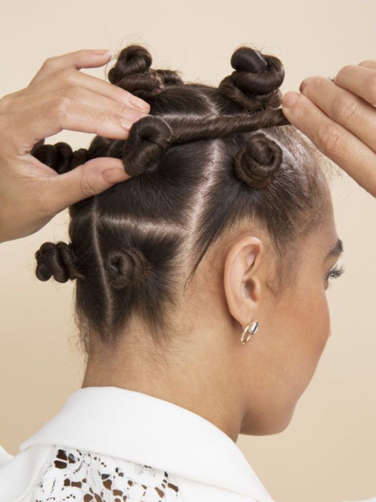 Woman with natural curls twisting her hair into a Bantu knot to match the 7 she already has.