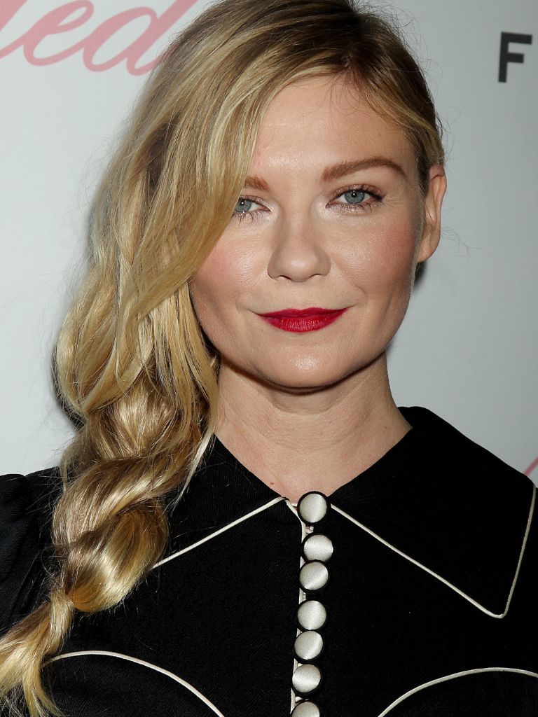 Easy hairstyles for fine hair: Kirsten Dunst with long golden blonde hair styled in a side twisted braid wearing a navy collared top.