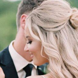 Half up half down wedding hairstyles: Woman with long bleach blonde curly styled into a half-up bun, posing outside.