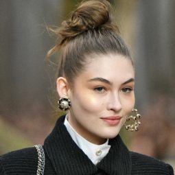 French hairstyles: Closeup shot of a woman with long hair in a high messy bun wearing a black coat on the runway