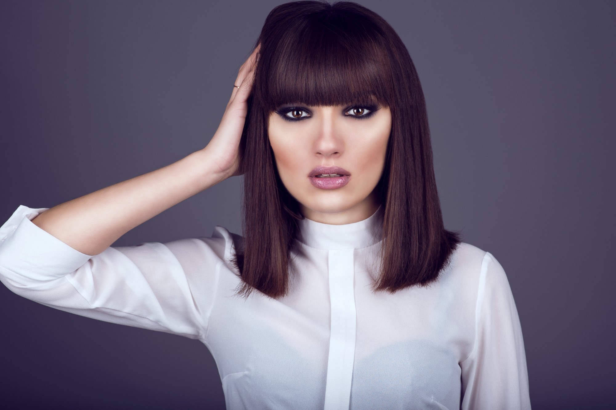 model is wearing heavy make up and has one hand on the side of her head