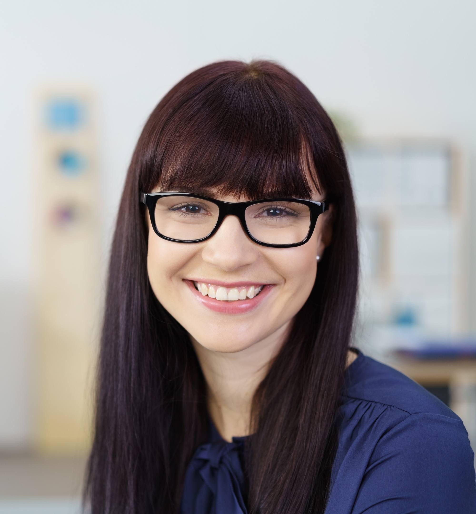 Styling blunt bangs: Closeup shot of a woman with long dark hair with bangs wearing eyeglasses