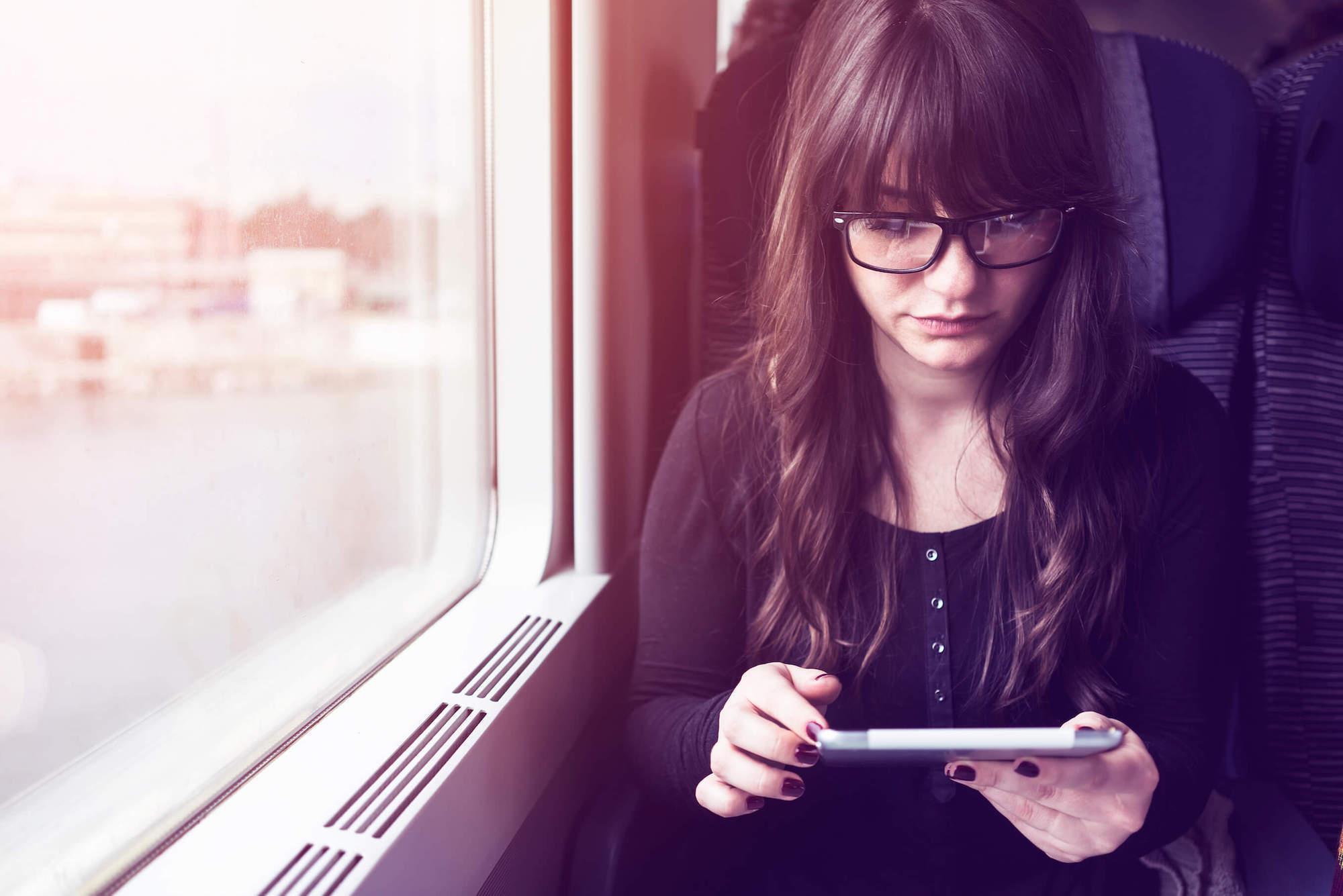 Should I get bangs: Girl on a train with long dark hair and blunt bangs with eyeglasses reading on her tablet