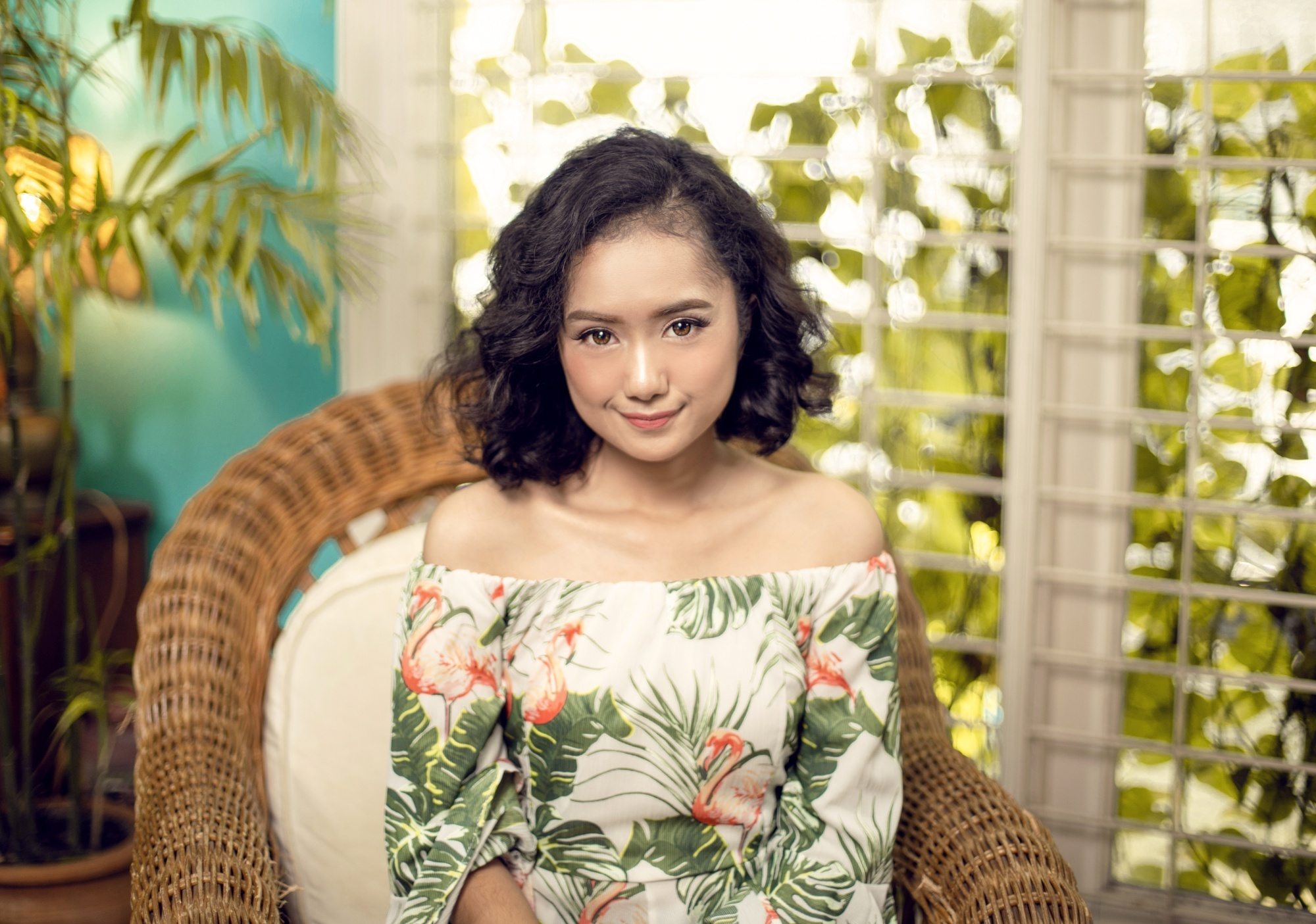 Asian woman with short hair curls sitting on a wicker chair