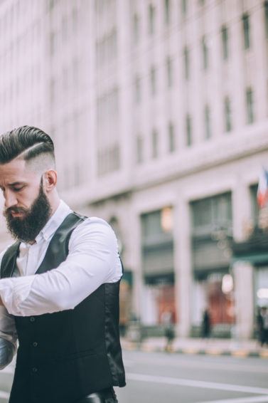 Retro looking businessman with hard part haircut going through the town dressed in formal wear, checking the time.