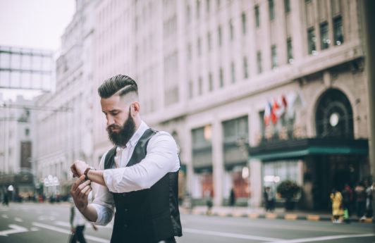 Retro looking businessman with hard part haircut going through the town dressed in formal wear, checking the time.