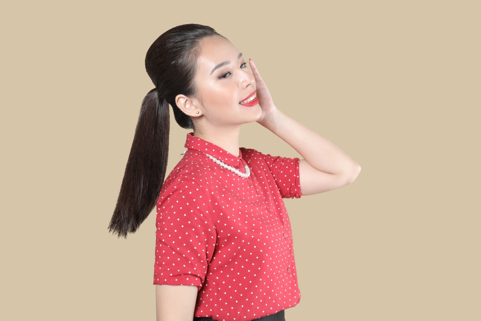Girl in a red top is slightly looking up and her hand is on her cheek