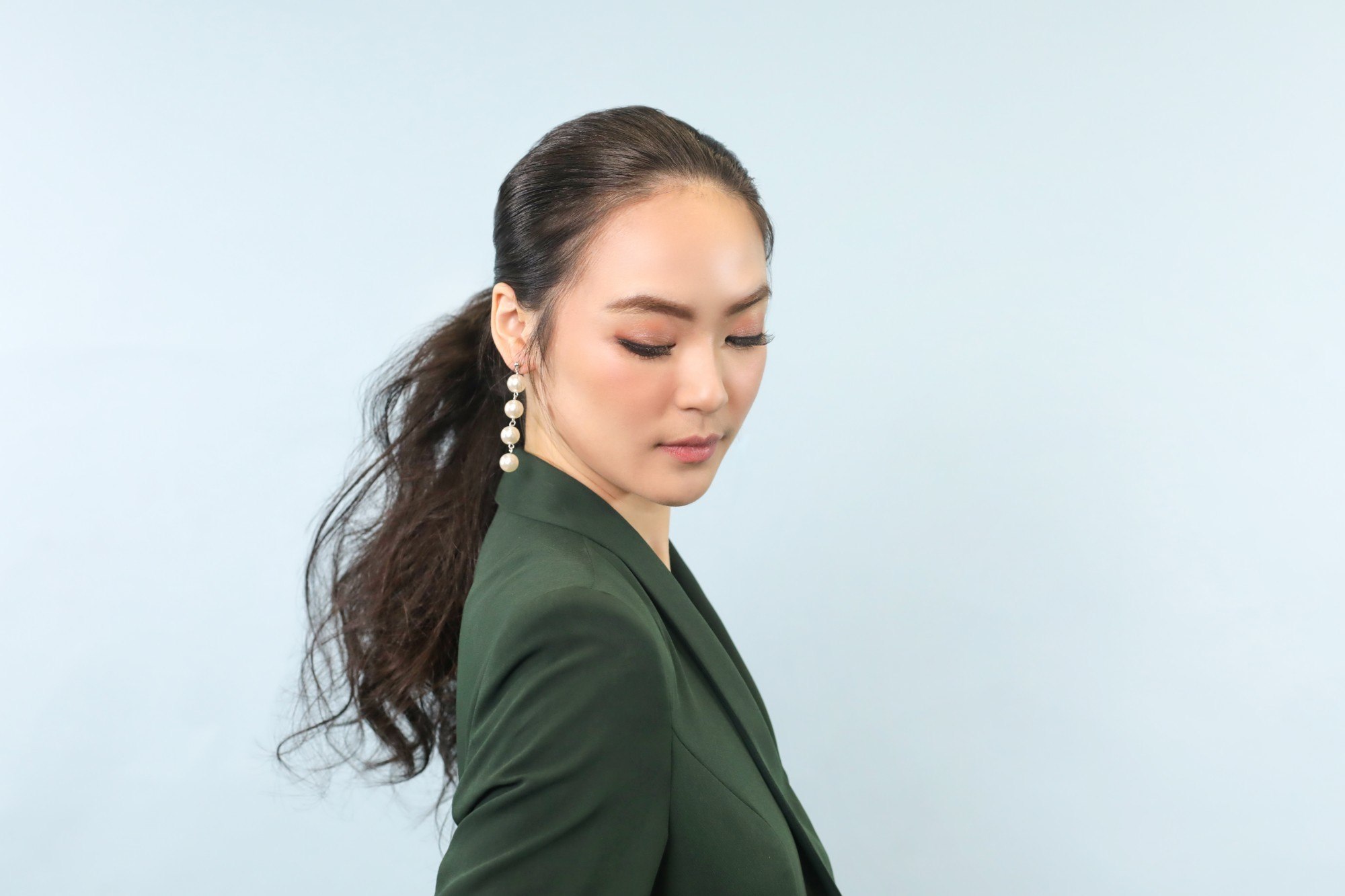 Girl wearing a green jacket and dangling earrings has a tousled ponytail