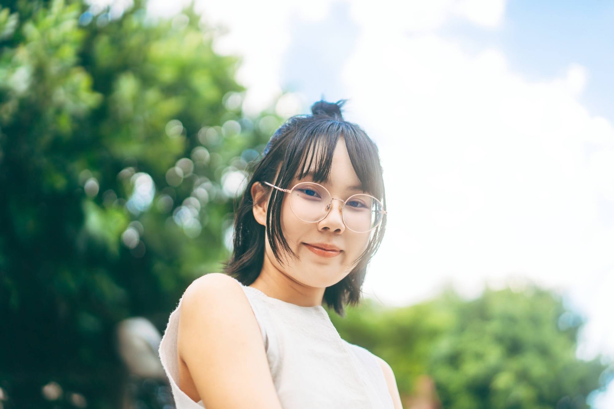 Asian woman with short hair and wispy bangs wearing eyeglasses and a white sleeveless top.