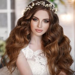 Curly wedding hairstyles: Woman with long brown curly hair wearing a wedding dress and flower crown
