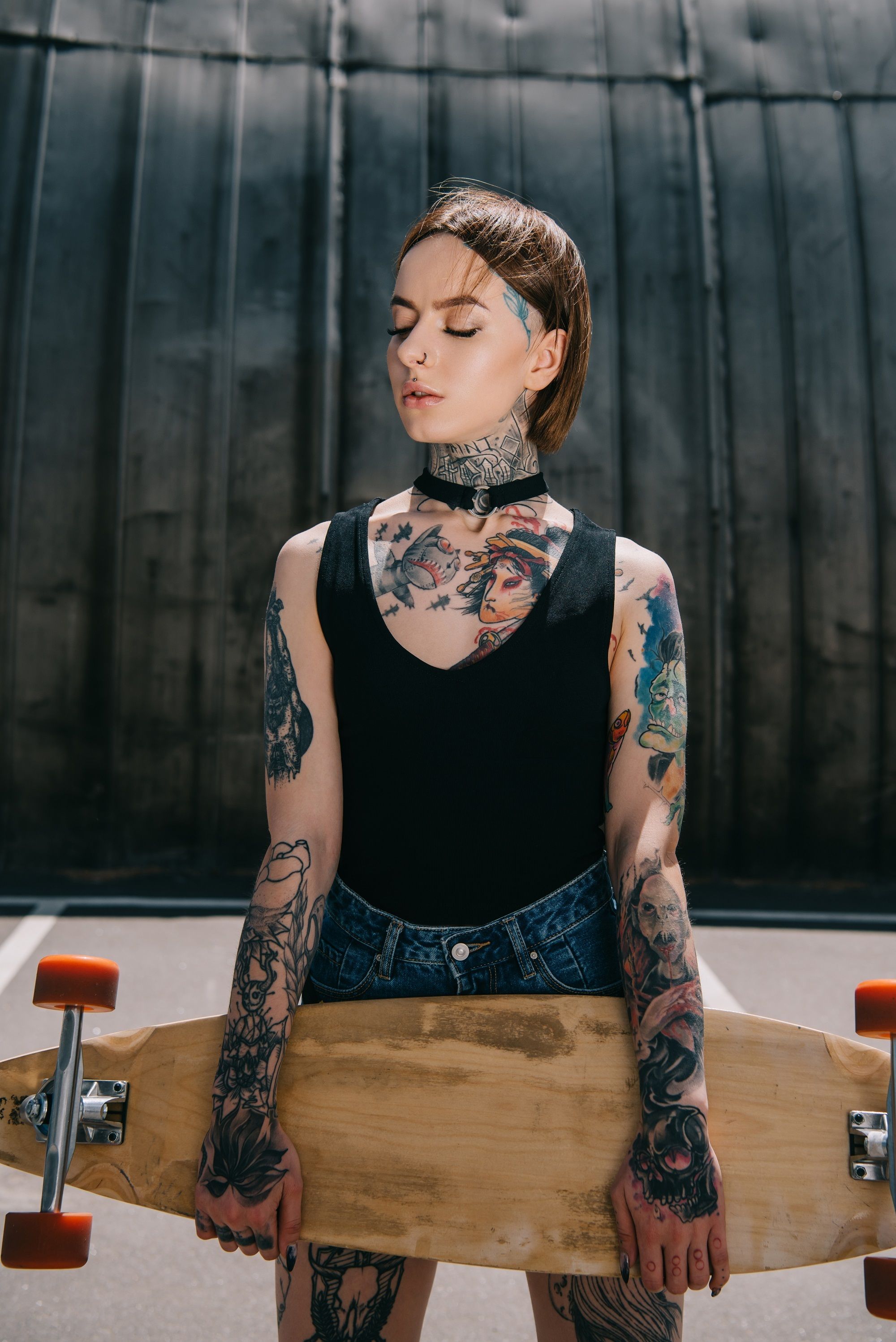 Hairstyles for skaters: Woman with slicked back bob and tattoos holding a skateboard