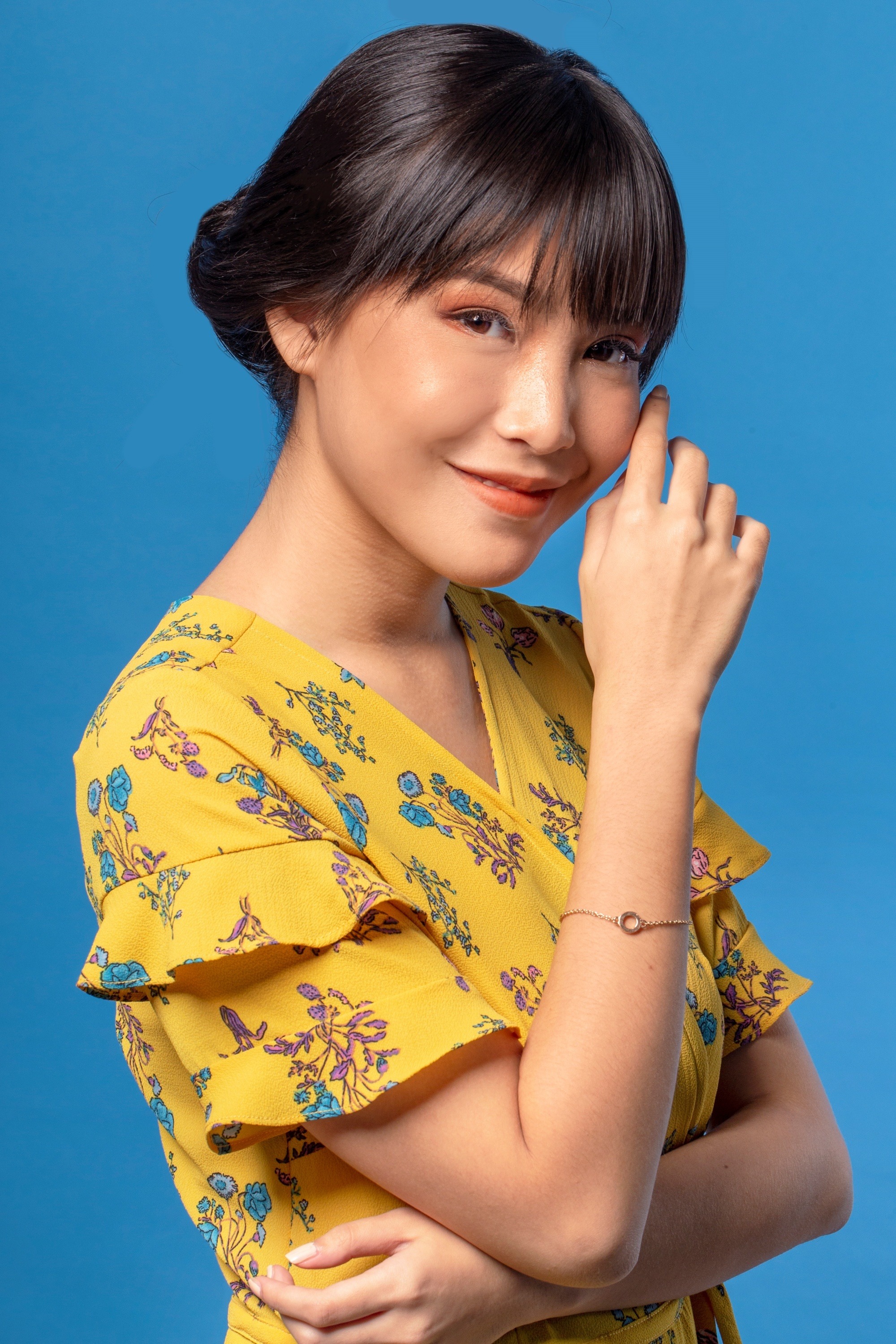 Closeup shot of an Asian woman with hair in a bun wearing a printed yellow dress