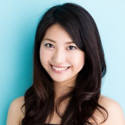 Best haircuts for long hair: Asian woman with long black wavy hair close up shot against a blue background